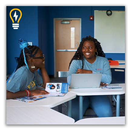 Two girls work together in a hybrid classroom using laptops